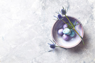 Colored quail eggs and sea holly flowers in a ceramic bowl (flat lay arrangement)
