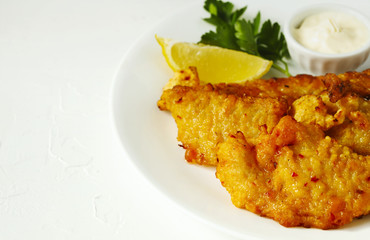 Golden batter deep fried fish fillets, served on white plate with sauce and lemon