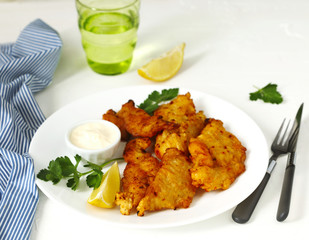 Golden batter deep fried fish fillets, served on white plate with sauce and lemon