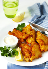 Golden batter deep fried fish fillets, served on white plate with sauce and lemon