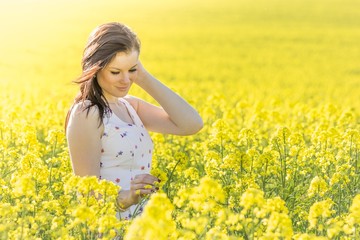 Fototapeta premium Beautiful youth woman with flower in summer meadow looking down. Beautiful girl eyes closed in yellow flowers field infinite horizon. Sunny sun sunshine and authentic lifestyle in windy weather hair