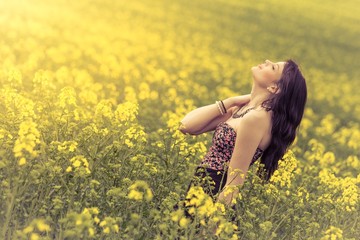 Naklejka na ściany i meble Beautiful woman in meadow of yellow flowers with head up. Attractive genuine young girl enjoying the warm summer sun in wide green yellow meadow. Experimental inclined plane. Part of series