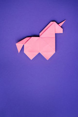 Handmade pink trendy geometrical origami unicorn on ultraviolet background. Empty copy space. Vertical poster, postcard, banner template.