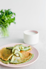 shrove, pink plate with green pancakes and kiwi, a glass of milk