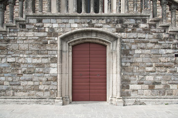 Fototapeta na wymiar Burgundy door in stone wall with elaborate frame