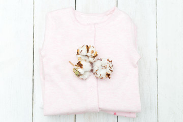 Baby eco-friendly clothing with cotton flower on wooden background. Flat lay