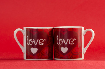 Two mugs with the word love and a little heart against red background. Valentine's Day