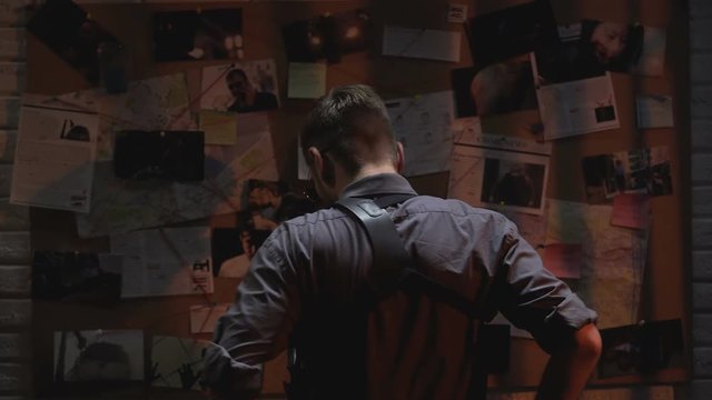 Cool male detective looking at investigation board, searching for solution