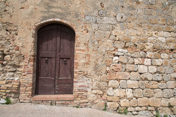 Fototapeta na wymiar Tilted narrow closed door in ancient stone wall 