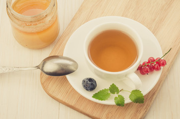 cup of tea with berries and mint in a saucer and honey/cup of tea with berries and mint in a saucer and honey on a wooden tray. Top view