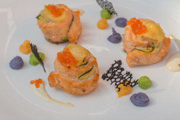 Baked salmon decorated with red caviar and colored sauce on white plate - seafood for gourmet. Selective focus.