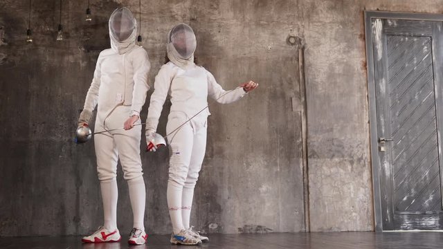 two athletes stand against the background of a modern wall, a woman and a man holding a sword or rapier for fencing, they compete in competitions
