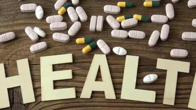 Pills with inscription HEALTH on brown wooden surface background