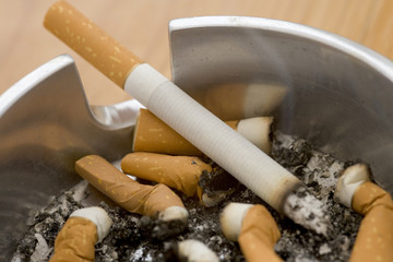 Ashtray full of extinguished cigarette butts with one lit
