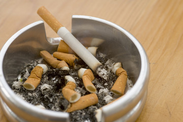 Ashtray full of extinguished cigarette butts with one lit