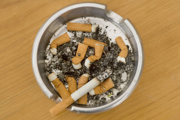 Ashtray full of extinguished cigarette butts with one lit