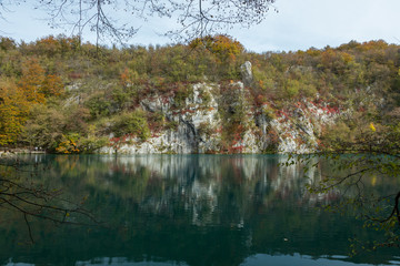 White cliffs in Plitvice Lakes National Park with a few tree branches in the shot. The reflection of the white cliffs can be seen in the still water. 