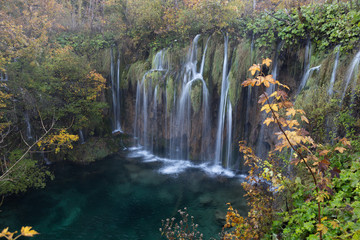 Long exposure of a waterfall in Plitvice Lakes National Park. There is lush foliage surrounding the waterfall and the water is crystal clear turquoise blue. 