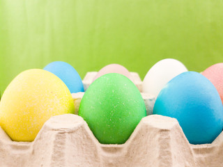Easter color eggs in paper box on green pastel background. Close up macro.