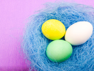 Easter color eggs in pastel blue nest on purple background. Close up minimalism style.