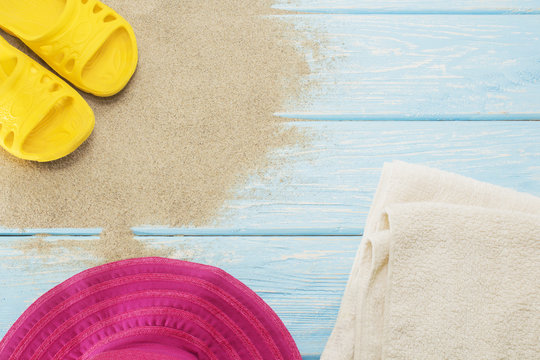 yellow flip flops on white beach sand, bright hat and towels.