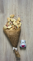 on a wooden table lies a pile of crumpled paper with cookies in the form of hearts and a pile of colorful and pyrofessional souffle in the form of a bear with a heart
