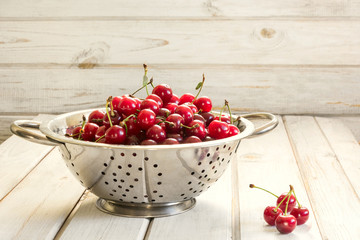 Metal colander full of freshly cherries over a rustic board.