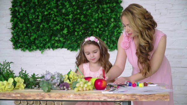 Mom and little daughter in dresses draw with pencils among flowers and fruits