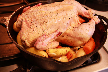 Raw chicken, seasoned and placed on top of vegetables and ready to be roasted in cast iron skillet. 