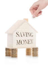 Wooden house model standing on coins and hand