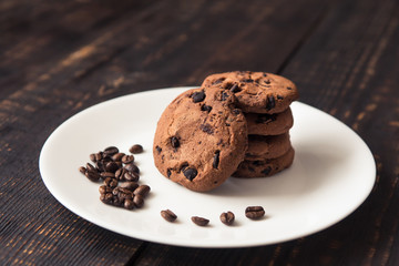 chocolate chip cookies on a white plate with coffee beans on dark wooden table