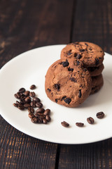 Fototapeta na wymiar chocolate chip cookies on a white plate with coffee beans on dark wooden table