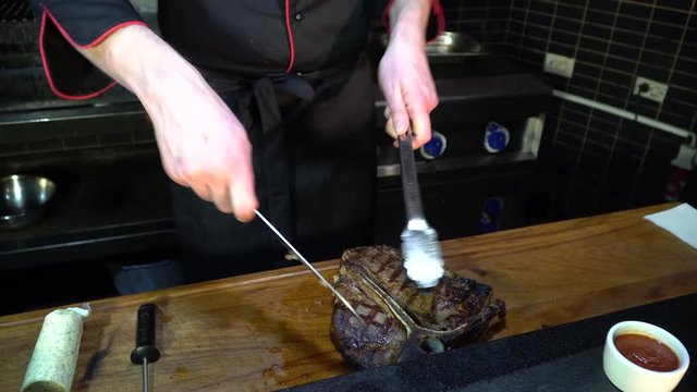the cook cuts the steak with a kitchen knife and tongs in the kitchen