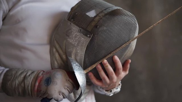 Close up shot of a professional swordsman holding mask and sword indoor. Costume looks old and used.