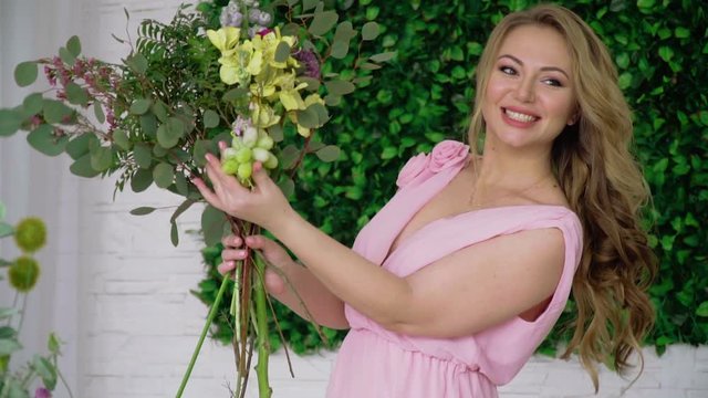 A woman florist is thinking of attaching a bunch of grapes to a bouquet
