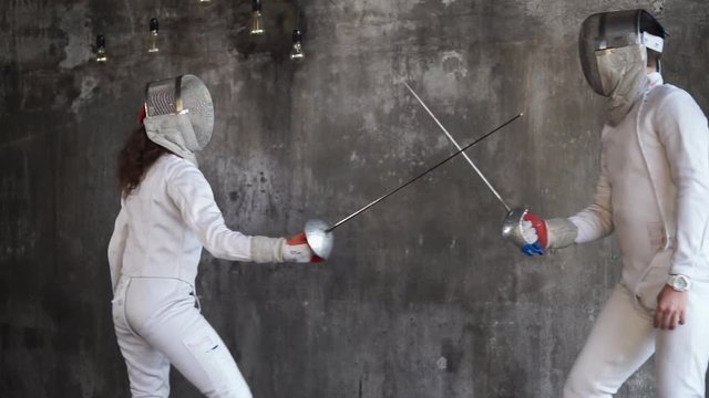 Two active and young athletes in a protective form are trained to engage in swords, fencers are engaged in a fitness club, coaching protection and attack