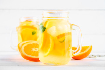 Orange detox water in mason jars on a white wooden table. Healthy food, drinks.