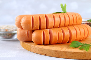 Fried chopped sausages on a wooden board on a gray concrete table.