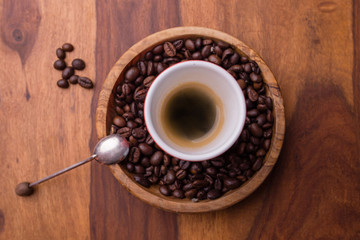 A cup of black coffee in the center of coffee beans with a spoon