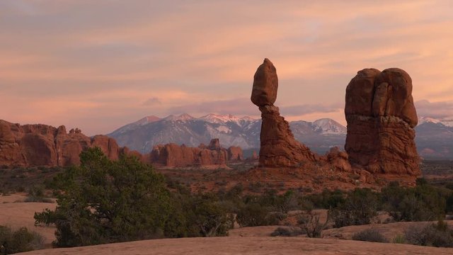 Revealing Balanced Rock during colorful sunset in the Utah desert while walking towards from behind hill.