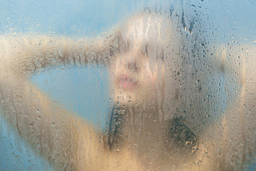 Rear view of unrecognizable female with naked perfect body takes shower, feels relief and pleasure, poses against blurred sweat glass surface of shower cabine. Skin care and relaxation concept