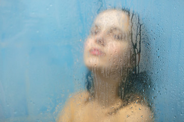 Nude female with wet hair poses in shower booth against blurred sweat background, feels relaxed as...