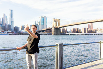 Young man outside outdoors in NYC New York City Brooklyn Bridge Park by east river, railing,...