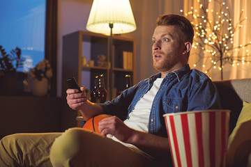 Amazed bearded man watching television while sitting on sofa in room. Rest concept