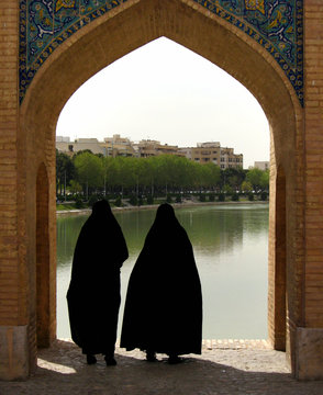 Two women wearing black chadors stand on Khaju bridge in Isfahan, Iran