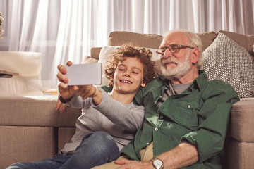 Portrait of cheerful grandfather and glad child taking selfie by phone. Entertainment concept