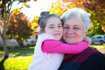 Happy family, generation and people concept - happy smiling young tree years old granddaughter with senior grandmother standing by House at Autumn Season, hugging in Oregon USA close-up portrait 