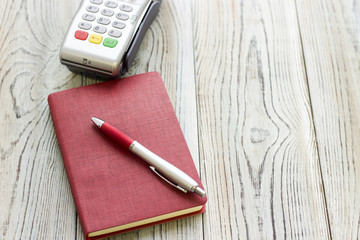 Modern technology and people concept - pos terminal, notepad and a pen. Rough bords background. Closeup