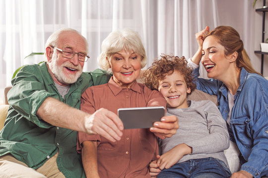 Portrait of happy grandpa, smiling child, glad grandmother and laughing mom taking selfie by mobile. Technology concept