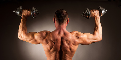 Fototapeta na wymiar Strong male athlete works out with dumbbells in studio over dark backgound